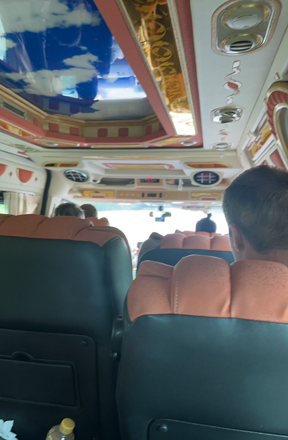 Inside the border-run bus — ornate Thai bus ceiling with painted sky mural