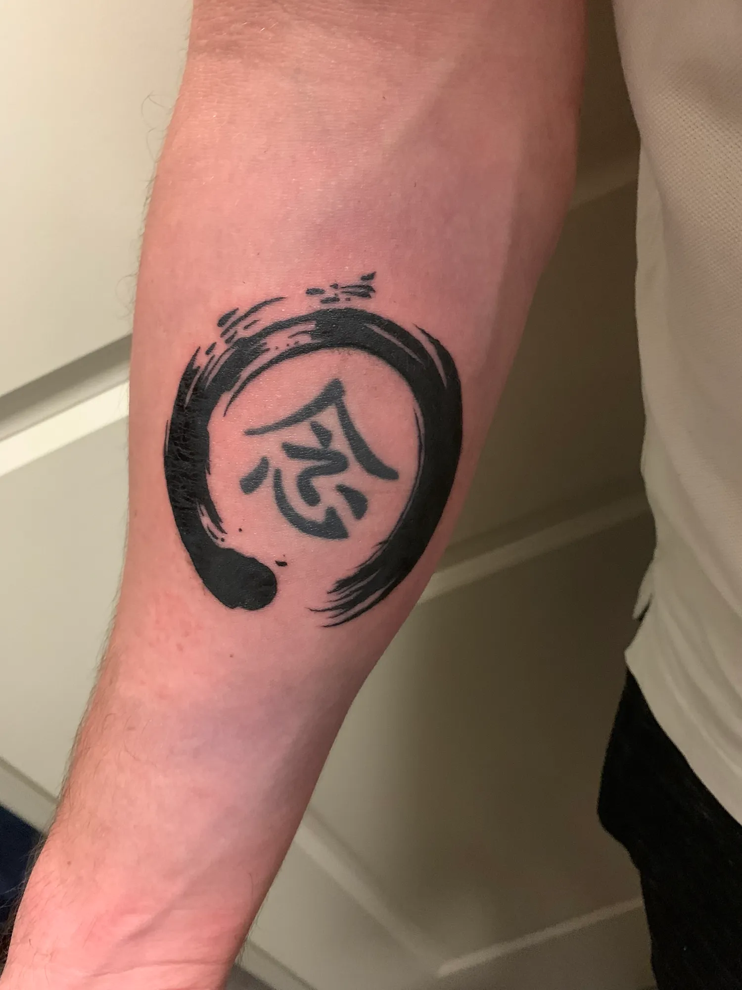 Ensō circle tattoo with a character at its centre, right arm
