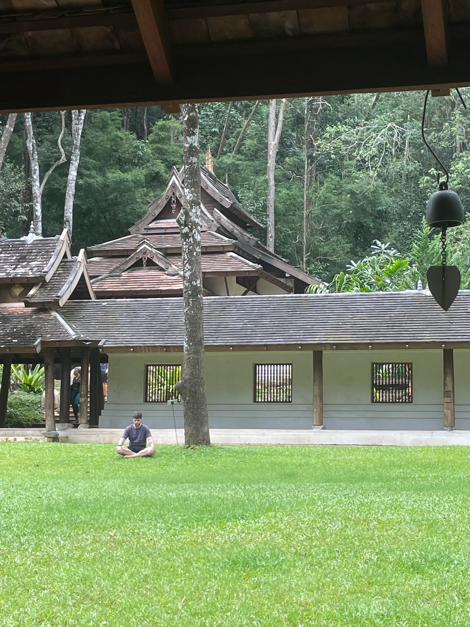 Wooden pavilions of a forest temple on Doi Suthep, with someone sitting on the lawn